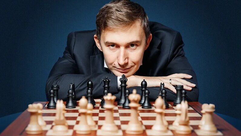 молодой шахматист, сосредоточенно смотрящий на доску на фоне часов