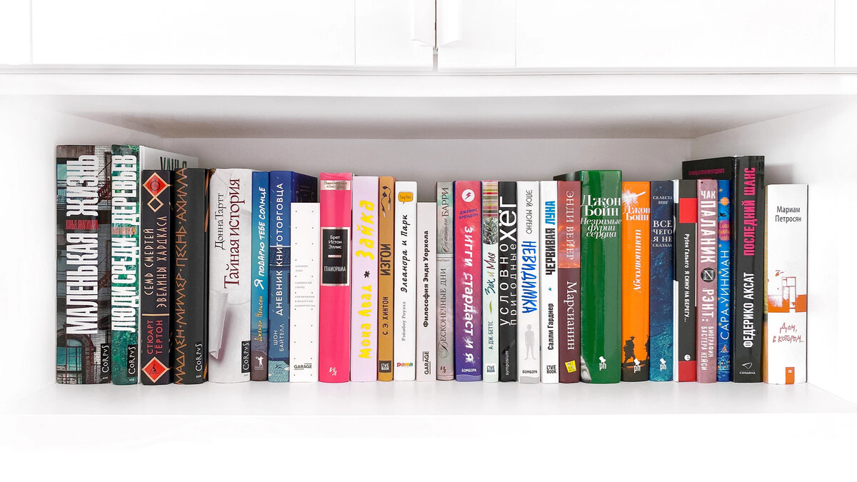 На книжной полке. Выбирает книгу. Книги самые топ.