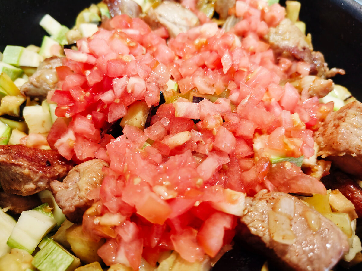 Добавление помидоров в сковороду с обжаренным мясом и овощами