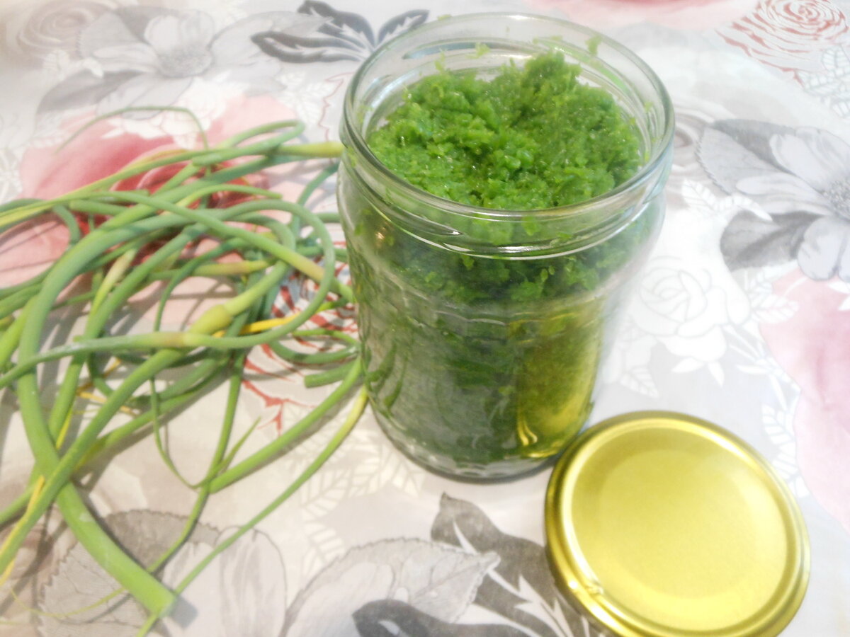 Счастливые обладатели огородов и приусадебных участков наверняка из год в год садят чеснок. Понятно, что ради ароматных головок, но возможно не все знают, что до цветения растения можно собрать еще один чудесный урожай – нарезать чесночных стрелок. Это просто изумительное лакомство, скажу я вам. Чего только стоят жареные стрелки чеснока – в готовом виде блюдо сложно отличить от ароматных жареных грибов. Многим нравится пикантная холодная закуска – маринованные стрелки чеснока. Но сегодня я хочу поделиться с вами заготовкой из стрелок чеснока на зиму.
Получается универсальная очень ароматная приправа - чесночная паста, которую можно использовать при приготовлении первых и вторых блюд, запеканок и даже выпечки. Даже просто смешав заготовку из стрелок чеснока с прокрученным соленым салом, вы получите ну очень вкусную и ароматную намазку на хлеб. В общем, пробуйте – это супер-заготовка на зиму!
Польза чесночной пасты:
Восстанавливает витаминно-минеральный резерв.
Обладает антимикробным действием и противогельминтными свойствами.
Стимулирует выработку ферментов, отвечающих за переваривание пищи и усвоение питательных веществ.
Улучшает кровоснабжение, повышает уровень гемоглобина в крови, останавливает формирование холестериновых бляшек. Предупреждает развитие анемии и атеросклероза.
Повышает общий тонус организма.
Снижает уровень сахара в крови.
Уменьшает вероятность формирования тромбов, разжижает кровь, снижает возможность заболеть варикозной болезнью.
Нормализует работу печени, стимулирует выделение желчных солей, купирует образование конкрементов в желчном пузыре и протоках.
Обладает слабым анальгезирующим и выраженным противовоспалительным действием.
