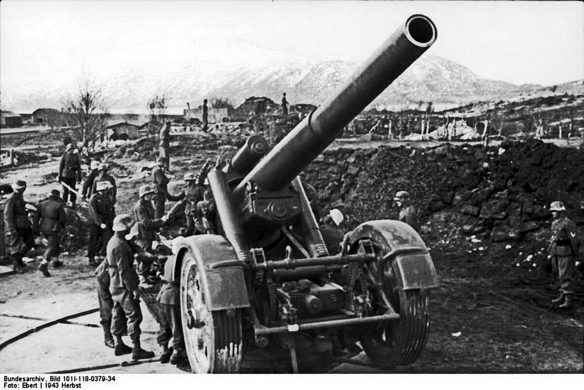 210-мм мортира Mrs 18 развёртывается расчётом на позиции. Видна большой высоты обваловка из насыпного грунта, под самой мортирой выровнена площадка для увеличения сектора обстрела по горизонту. 1943 г.