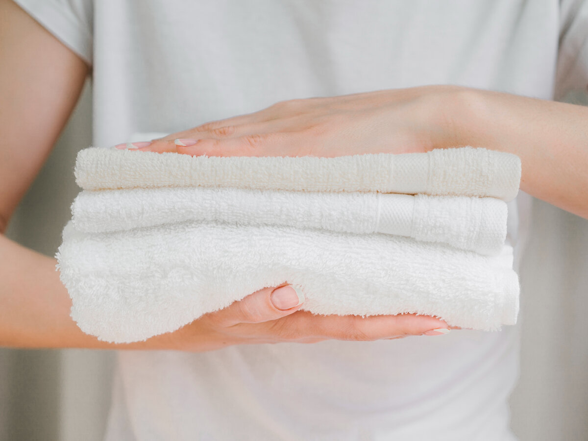 Белоснежное полотенце в руках. Чистые полотенца в руках девушки. Полотенце между пальцев. Различия между полотенцами. Воняют полотенца