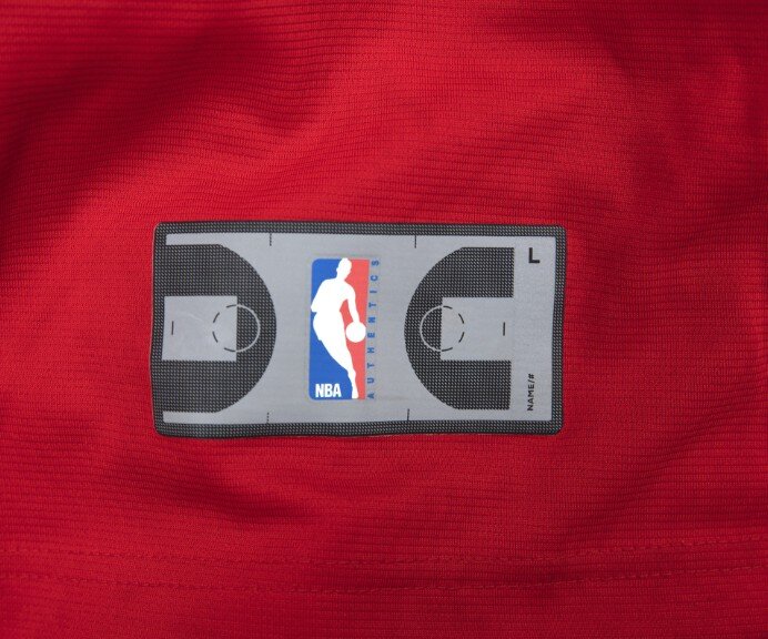 На бирке NBA, расположенной в нижней части майки Replica, изображен логотип NBA, наложенный на баскетбольную площадку. (Адди Блэкер)