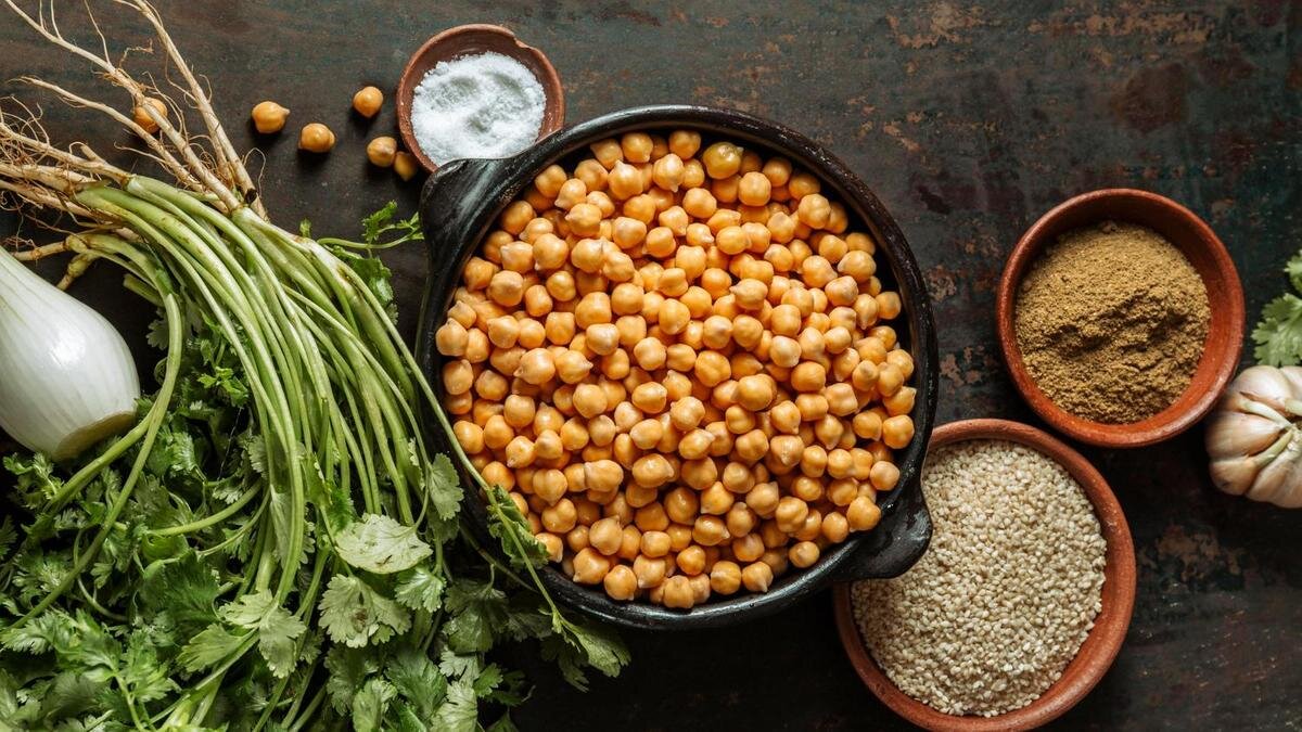    В центре стола стоит тарелка с нутом, рядом кунжут, петрушка и специи:Freepik