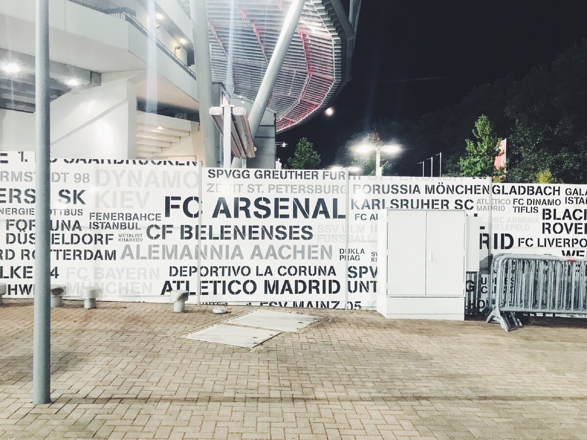 Вход на гостевую трибуну огорожен таким забором — с названиями команд, которые играли на этом стадионе 