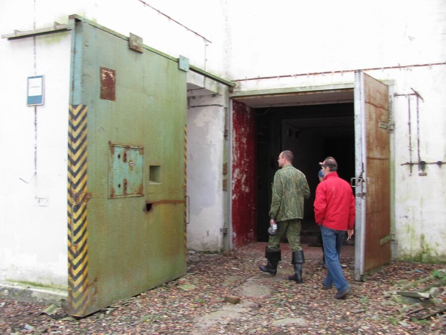  Заходим в "курятник" и осматриваемся. Прямо перед нами распахнутая металлическая створка ворот главного входа в хранилище. Слева сдвижные металлические ворота, прикрывающие вход в хранилище для обслуживающего персонала. В этих воротах предусмотрено окошко для часового. Оборачиваемся и видим справа еще одно небольшое техническое помещение со снятыми дверями. В нем пусто. По всей видимости оно связано с обслуживанием "курятника" и кран-балки. 