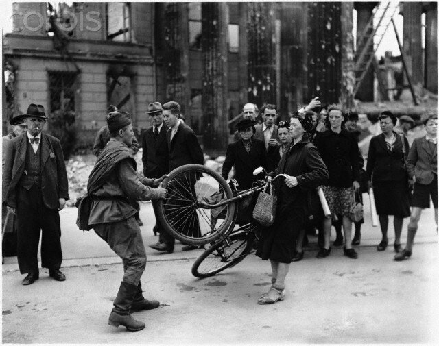 Советский солдат отнимает у немки велосипед (по мнению одниx), или советский солдат помогает немке выровнять руль (по мнению другиx). Берлин, август 1945 года.