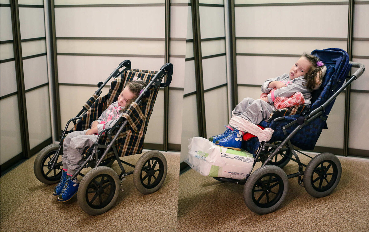 Обе коляски выдали Маргарите в Протезно-ортопедическом восстановительном центре. Слева — коляска, которую делали восемь месяцев по индивидуальному заказу. Должна была раскладываться, но не раскладывается. Справа — стандартная коляска, которую тоже выдали бесплатно. Чтобы ее хоть как-то использовать, мама девочки придумала систему валиков, подушек, ремешков и завязок, которые фиксируют ребенка в нужном положении. Эта коляска служит Маргарите стульчиком для кормления. Фото: Сергей Гудилин, Имена