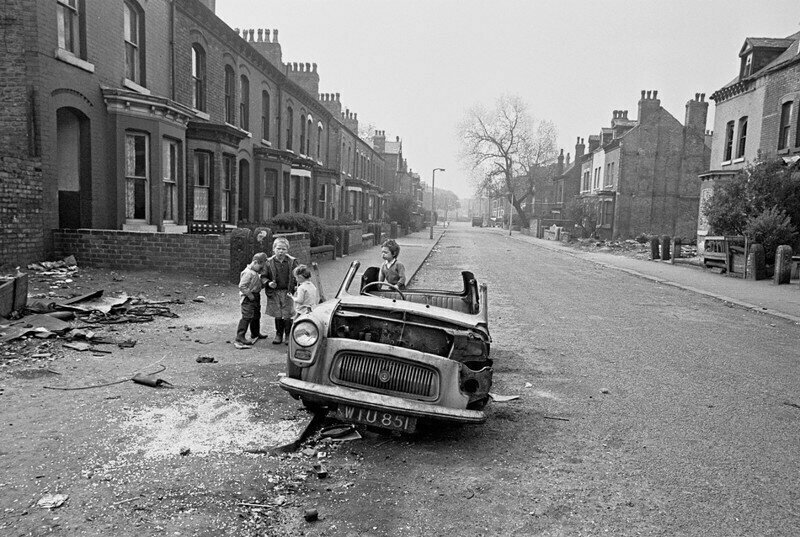 Manchester, 1970. Children play in a wrecked car on the street.