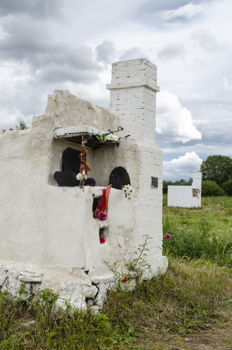 На месте каждой сожженной избы установлена печь, у очага размещены остатки утвари, люд приносят цветы и игрушки