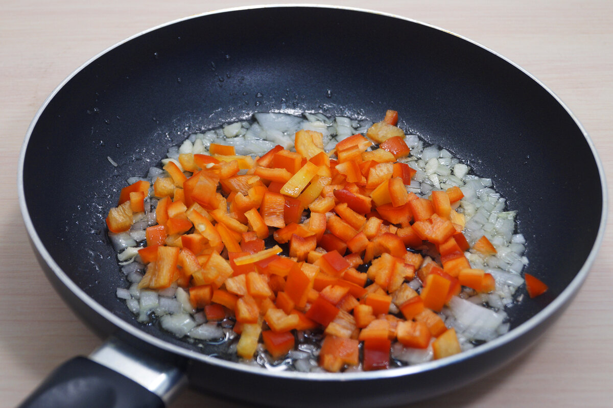 Добавить половину мелко нашинкованной луковицы и 2 измельченных зубчика чеснока. Добавить кубиками нарезанный болгарский перец. Обжарить, помешивая, 2-3 минуты.