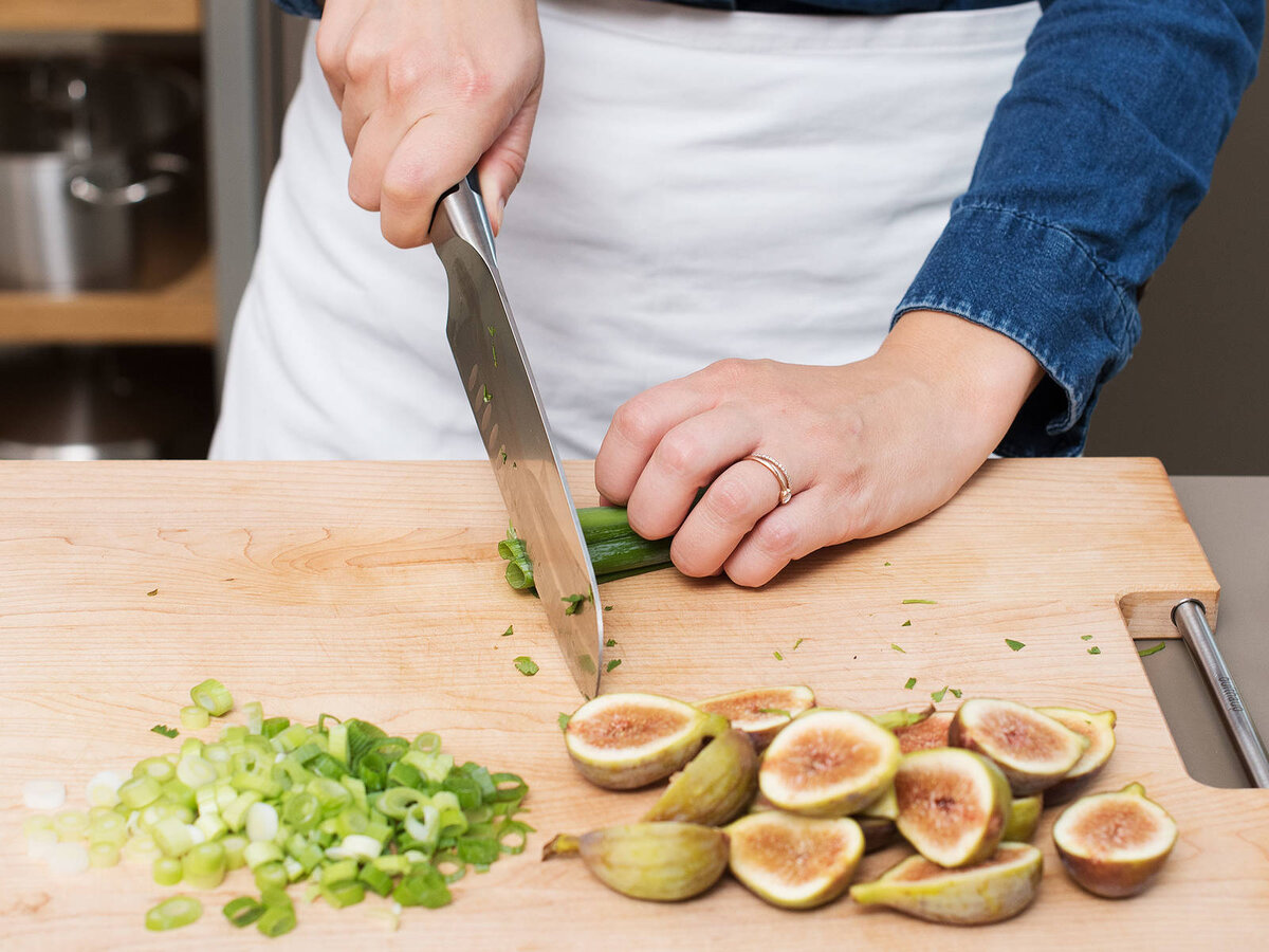 1. Разогрейте духовку до температыры 180°C и выстелите противень пергаментной бумагой. Разрежьте инжир пополам. Помойте зеленый лук, нарежьте тонкими кольцами. Мяту и кинзу помыть, обсушить, мелко нарезать. Покрошите Фету и очистите зерна граната.
