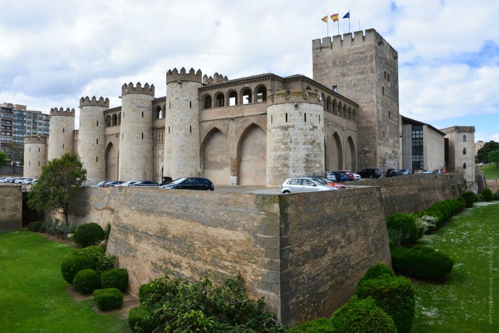 01. Я приехал сюда прямиком из Бильбао (всего-то 4,5 часа на региональном поезде). Железнодорожный вокзал Zaragoza-Delicias находится на окраине города, впрочем до центра отсюда всего 3-4 км. Имеет смысл пройтись пешком, тем более что на пути можно встретить этот чудесный дворец Альхаферия, построенный в мавританском стиле примерно в XI веке. Впрочем, древнейшая (и крупнейшая) Башня Трубадура начала застраиваться еще в середине IX века. После мавров, стены замка были приспособлены под дворец католических королей. А в наши дни - это цитадель Кортесы Арагона (парламента).

