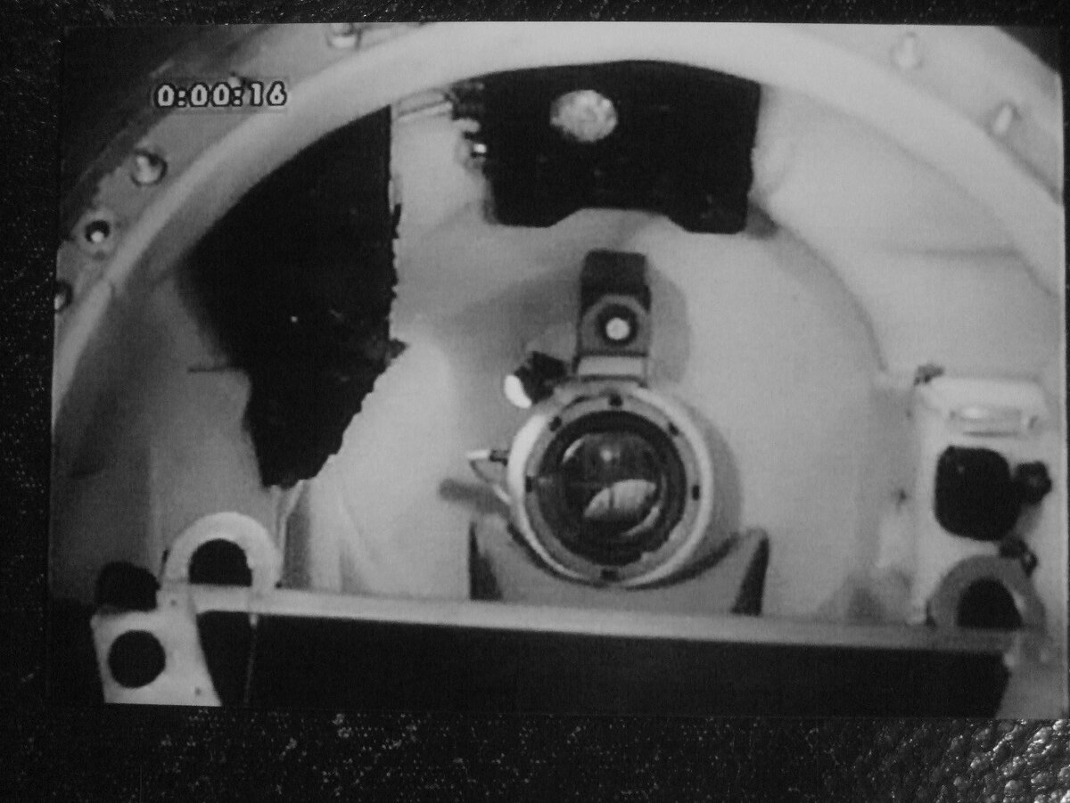 Кабина космического корабля «Восток-3А», используемая как тренажёр (входной люк снят). Посередине видно сложное оптическое устройство — иллюминатор «Взор». Через него космонавт в полёте видел не только то, что прямо перед «Взором», но и довольно широкое пространство вокруг него. Над ним размещена телевизионная камера. Справа — рукоятка управления. Сверху — пульт управления космическим кораблём. Слева — пульт управления тормозной двигательной установкой (ТДУ) Снизу видна спинка катапультного кресла. Фотография сделана через входной лю