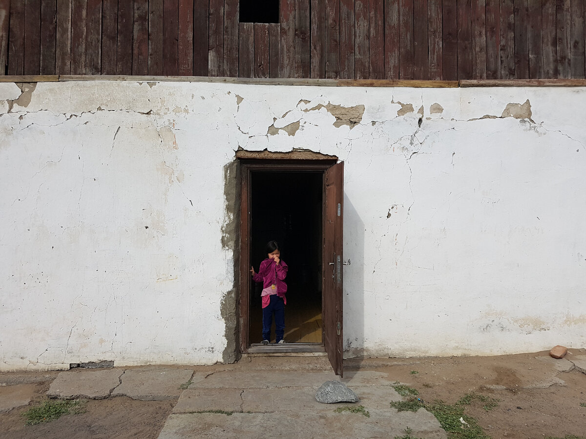 Попрощались с гостеприимным посёлком Тэс. К нам вышли знакомые Георгича, которые всё не могли поверить, что мы уже уезжаем, едва только приехав вчера вечером. И вот эта девочка в тот момент показалась в дверях, я не смог удержаться, чтоб не сделать это фото. Вообще, дети в Монголии - это удивительное явление. Благодаря рассказам Георгича, я узнал, что в монгольском обществе совершенно по-другому устроен процесс воспитания детей. С одной стороны, их невероятно оберегают, не ругают, не читают нотаций и, упаси, поднять на ребёнка руку, это исключено абсолютно. С другой стороны, они вливаются во взрослую жизнь гораздо раньше, чем это принято в европейском обществе. Уже с малых лет они включены в очень многие бытовые жизненные процессы.