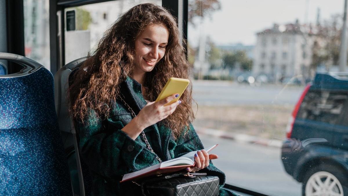    Девушка с вьющимися волосами сидит в автобусе и смотрит в телефон:Freepik/Freepik