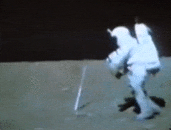    На видео мы видим как некто в костюме напоминающем скафандр пытается поднять 
с грунта свой молоток, кирку по сути.
Это его последняя попытка, до этого он безуспешно пытался это сделать,
но ему всё время что-то мешало опуститься вниз.
И, обратите внимание, согнуть на секунду колени он смог только после того, как подпрыгнув вверх зачем-то, по сути шлёпнулся всей массой о грунт.
То есть просто опуститься, согнув колени,  у него не было никакой возможности.