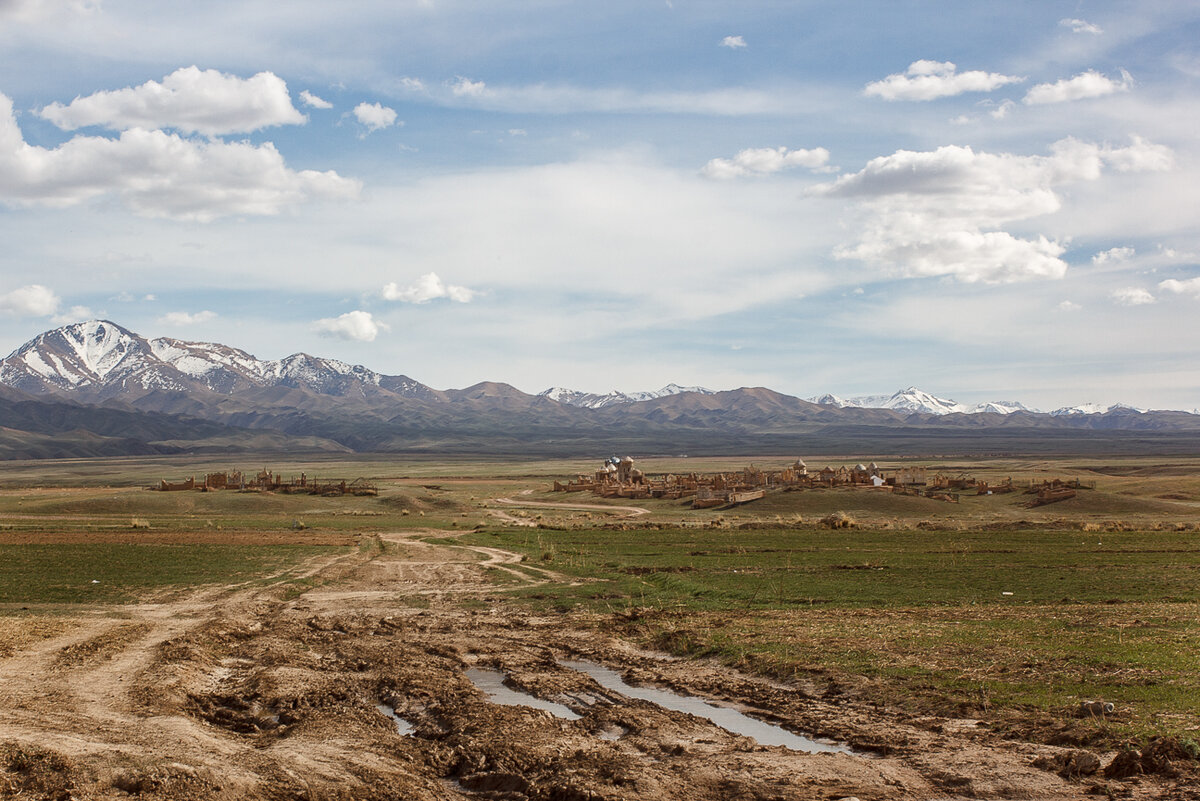 Размытая грунтовка и традиционный погост на фоне гор.