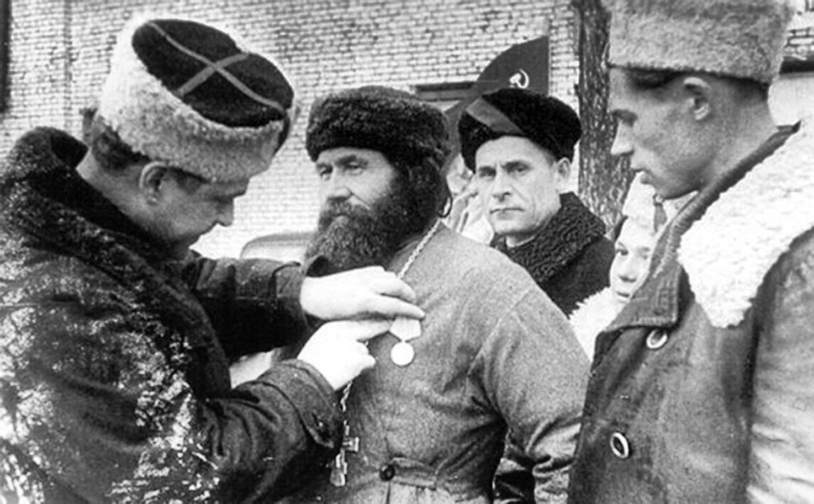 командир 5-й Ленинградской партизанской бригады, Герой Советского Союза К.Д. Карицкий прикрепляет медаль «Партизану Отечественной войны II степени» священнику церкви псковского села Хохловы Горки  Фёдору Пузанову. 
