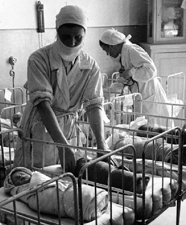 Медицинские сёстры укладывают новорождённых в кроватки в детской комнате родильного дома имени профессора Снегирёва, 1942 г. (Автор фото не установлен)