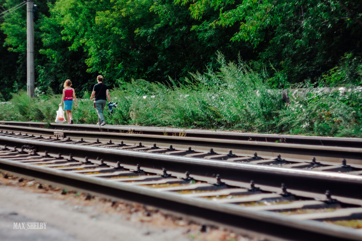 На 1 фото рельсы и столб подводят нас к двум прохожим. На 2 фото столб и отбойник к сидящему на нем малчьчику.