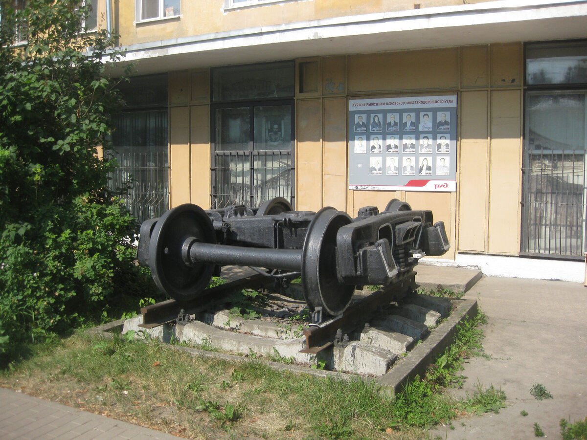 Вагонная тележка, установленная своеобразным памятником (Псков). У колёсной пары на переднем плане нас будет интересовать ограничительный гребень – реборда, что выступает за колесо с его внутренней стороны. И профиль «поверхности качения» самого колеса – отлично видно, что поверхность качения колеса явно коническая. Заодно, на срезе, видно форму головки рельса. Которая сделана под форму колеса и реборды. Их скругления более-менее совпадают. Фото автора.