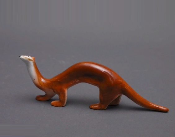 "Ласка", 1937. Фаянс. Фигура идущей ласки с длинным опущенным хвостом, с поднятой и повернутой чуть влево мордой. Раскраска коричневато-рыжая с белым. Размеры: 5,5*16,0 см. Номер в Госкаталоге 7296814. Государственное бюджетное учреждение культуры города Москвы "Музей-усадьба "Кусково". Изображение взято с сайта Госкаталог(точка)РФ. Листайте галерею вправо.
