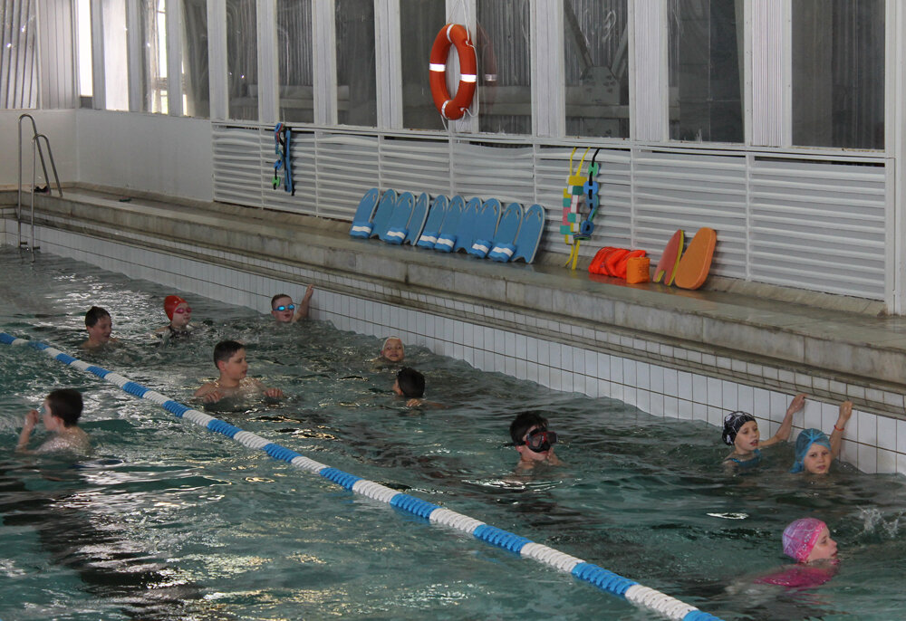 Группа младших школьников во время заключительного занятия. На стене наготове висят безопасные плавсредства 