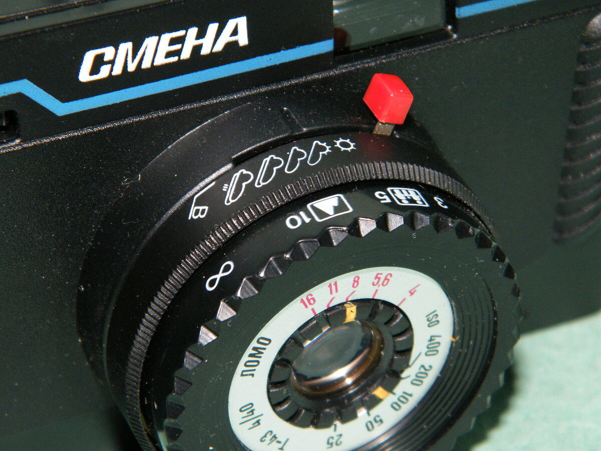 На этом фотоаппарате стоит объектив «Триплет». Часто его обозначали только одной буквой «Т». Завод-изготовитель — «ЛОМО» — Ленинградский оптико-механическое объединение.