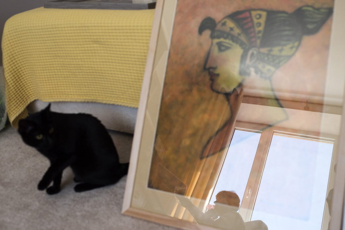 Ирина в отражении своей работы. Рядом сидит кошка Соня. Фото: Дарья Козырева для ТД