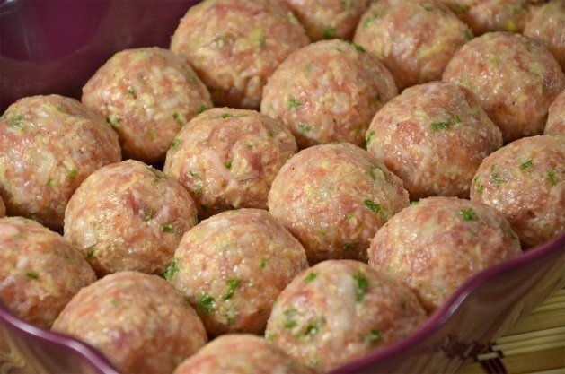 Приготовление:  
1. Сыр натрите на мелкой терке, одну луковицу мелко порежьте, рис отварите до полуготовности, а зелень измельчите ножом. 
2. Все компоненты вместе с солью и черным перцем добавьте в фарш и аккуратно перемешайте. Следите за тем, чтобы сыр распределялся по всей массе равномерно, не образуя комков. Вбейте яйцо и хорошенько вымесите готовый фарш. 
3. Очистите и нарежьте на небольшие кубики вторую луковицу и подготовьте чеснок. 
4. Лук выложите на сковороду с прогретым растительным маслом и доведите его до прозрачно-золотистого состояния. 
5. Если вы имеете дело со свежими помидорами, очистите их от кожуры и нарежьте аккуратными кубиками. Добавьте помидоры (или томатный сок) к жарящемуся луку и потомите соус под крышкой на слабом огне около 10 минут. Не забудьте посолить смесь, добавить сахар, чтобы убрать излишек кислоты и приправить соус черным перцем или паприкой. 
6. Отключите огонь под сковородой и только после этого добавьте в томатный соус порубленный чеснок. 
7. Смажьте дно формы для выпекания небольшим количеством масла и принимайтесь за приготовление тефтелей. Чтобы избежать прилипания фарша к рукам, смачивайте время от времени ладони в воде. 
8. Подготовленные мясные шарики залейте томатным соусом и отправляйте тефтели в разогретый до 180–200 ºC духовой шкаф. 
9. Через 30–40 минут откройте духовку, засыпьте тефтели оставшимся натертым сыром и прогрейте блюдо еще минут 10. 
10. Тефтельки идеально сочетаются с любым гарниром: отварным рисом, макаронными изделиями или картофелем. 

Приятного аппетита!