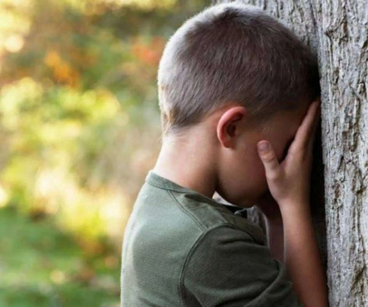 Сын плачет по отцу. Грустный ребенок. Печальный мальчик. Грустный мальчик. Мальчик прячется за деревом.