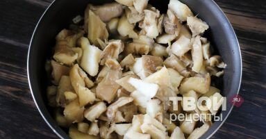 Грибы промыть, нарезать средним кубиком и высыпать в емкость к отпассерованной луковой нарезке. Всыпать 2 щепотки соли и 2 щепотки молотого черного перца. Обжарить в течение 7-10 минут, пока не выпарится жидкость из грибов и они не приобретут золотистый цвет.