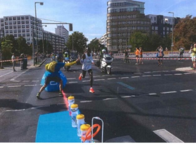 Сопровождающий "кормилец" подаёт Элиуду Кипчоге бутылку на одном из пунктов питания