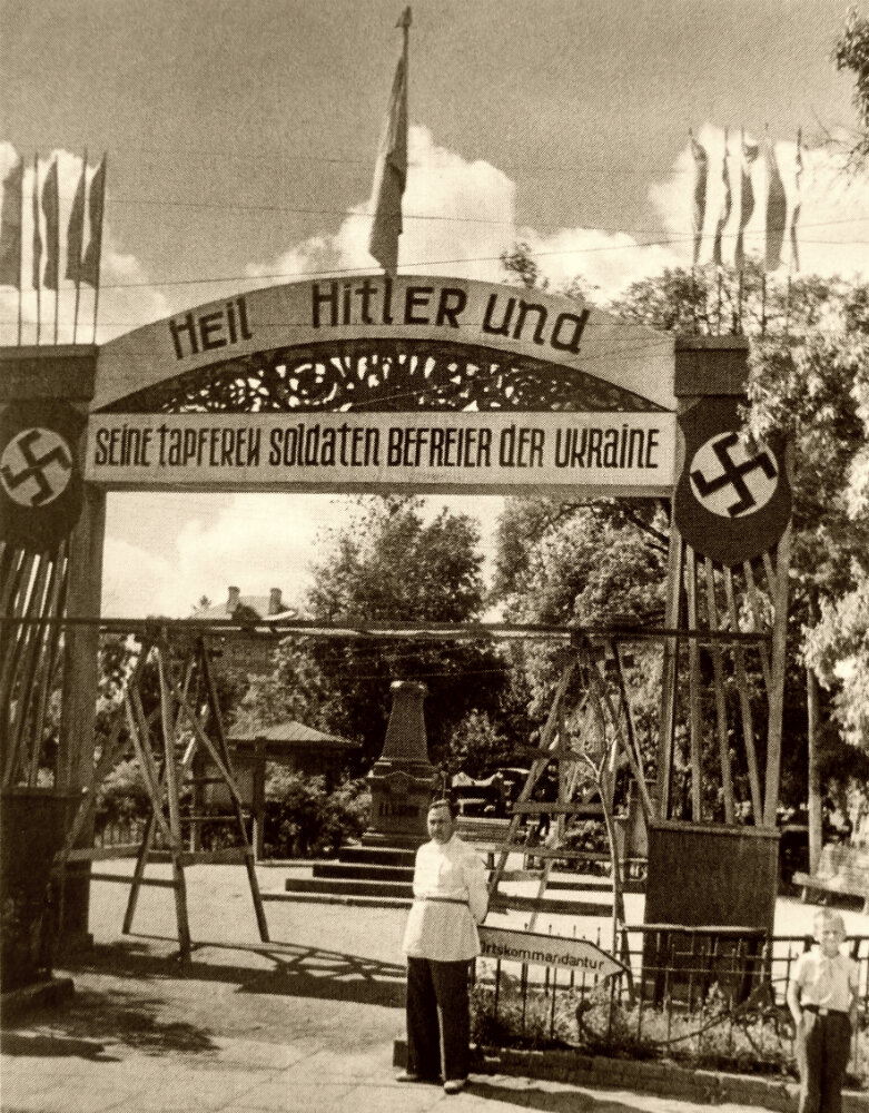 Жители оккупированного города на Украине стоят рядом с аркой с надписью на немецком языке: «Heil Hitler und seine tapferen Soldaten, Befreier der Ukraine» («Хайль Гитлер и его храбрые солдаты, освободители Украины».