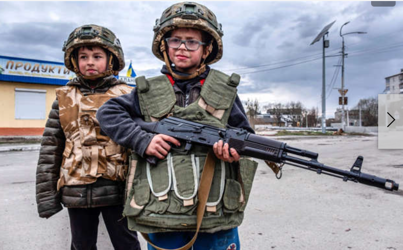 Первая леди Украины Елена Зеленская заявила в среду, 20 июля 2022 года, что продолжающаяся война России в Украине привела к тому, что ее маленький сын потерял интерес к прошлым увлечениям и подтолкнула его к желанию стать военным. 
Два мальчика в военных жилетах и касках помогают на военном контрольно-​пропускном пункте 4 мая 2022 года. Один из детей держит АК-47.
