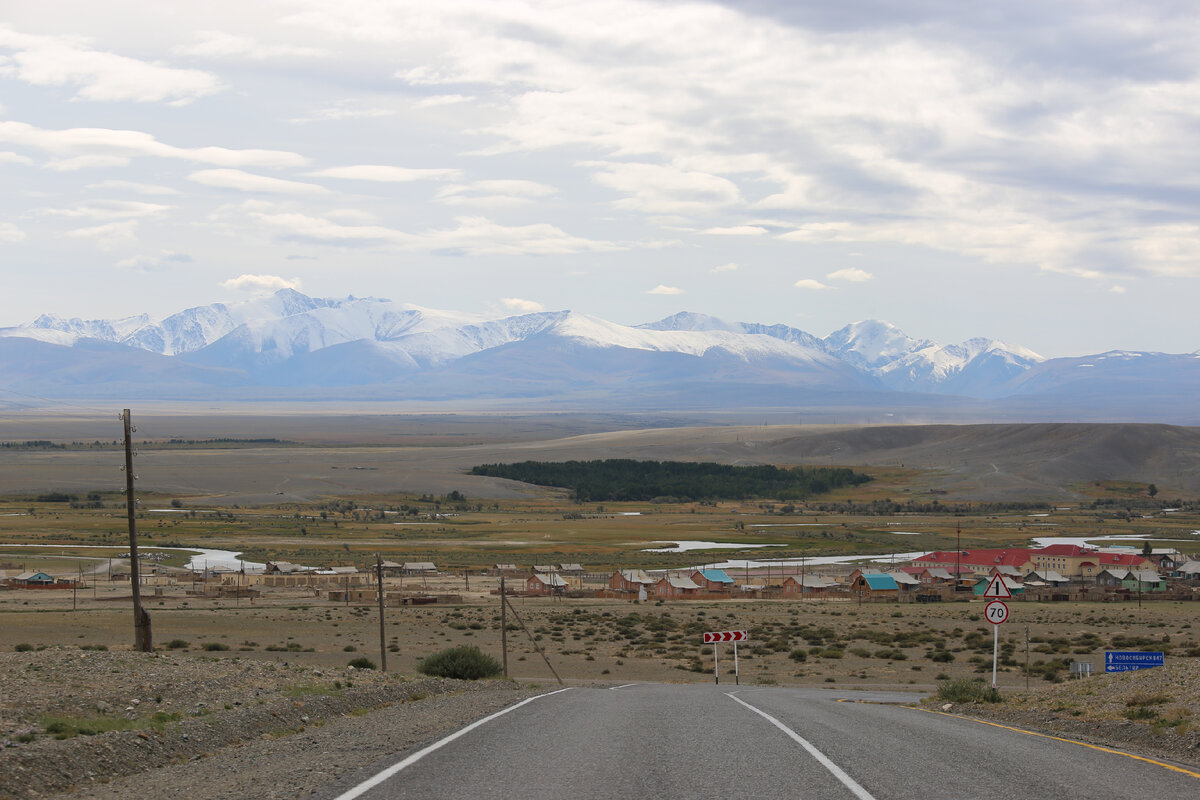 Просторная Курайская степь, над которой возвышаются снежные вершины Северо-Чуйского хребта. Где-то там гора Актру и на ней ледник Актру. Справа внизу виден синий дорожный указатель Бельтир на уже несуществующую деревню, полностью разрушенную землетрясением 2003 года.