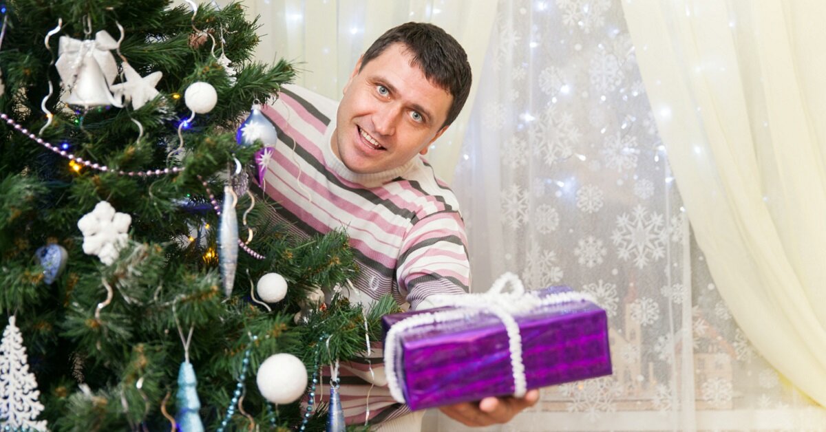   The man holds a gift at the Christmas tree in home interior Вита Сторож