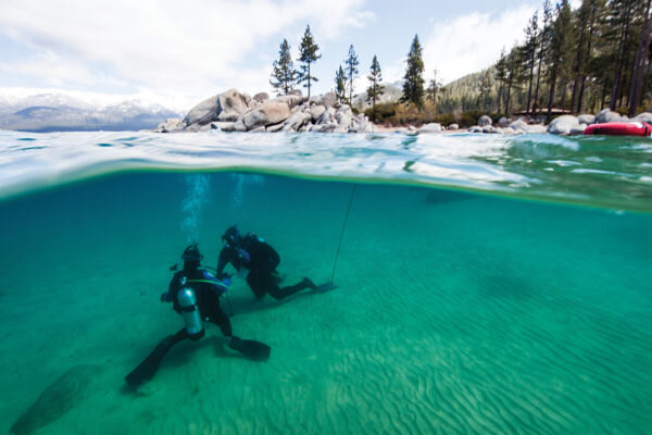 ИНСТРУКТОР ДАЙВ-ЦЕНТРА TAHOE ОБУЧАЕТ СТУДЕНТА В ХОЛОДНЫХ АПРЕЛЬСКИХ ВОДАХ DIVERS COVE ВОЗЛЕ SAND HARBOUR.