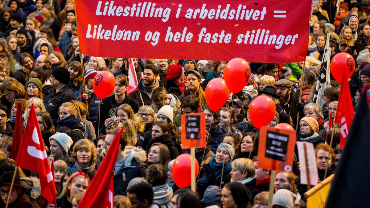 Надпись на транспаранте "равенство на рабочем месте = равная оплата труда и равный доступ к полной занятости"