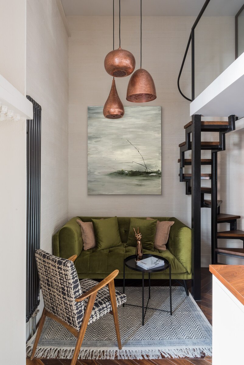 Фото: Ольга Мелексцева; стилист: Екатерина НаумоваГостиная. Диван сделан на заказ в мастерской Сергея Корба; над ним картина, написанная Александрой Ермиловой; кресло винтажное; декоративные подушки и ковер, Zara Home; светильники Ajour, Arte Lamp; журнальный столик, IKEA; на нем аксессуары, Moon-stores.