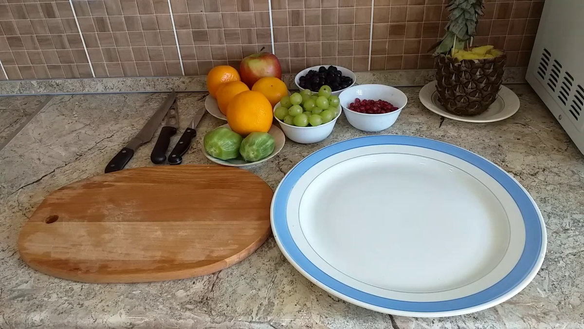 Нужно приготовить фрукты: апельсины, киви, виноград зеленый и черный, яблоко, гранат, мандарины. Киви почистить, остальные фрукты хорошо промыть. Приготовить тарелку, в которую мы будем укладывать фрукты.