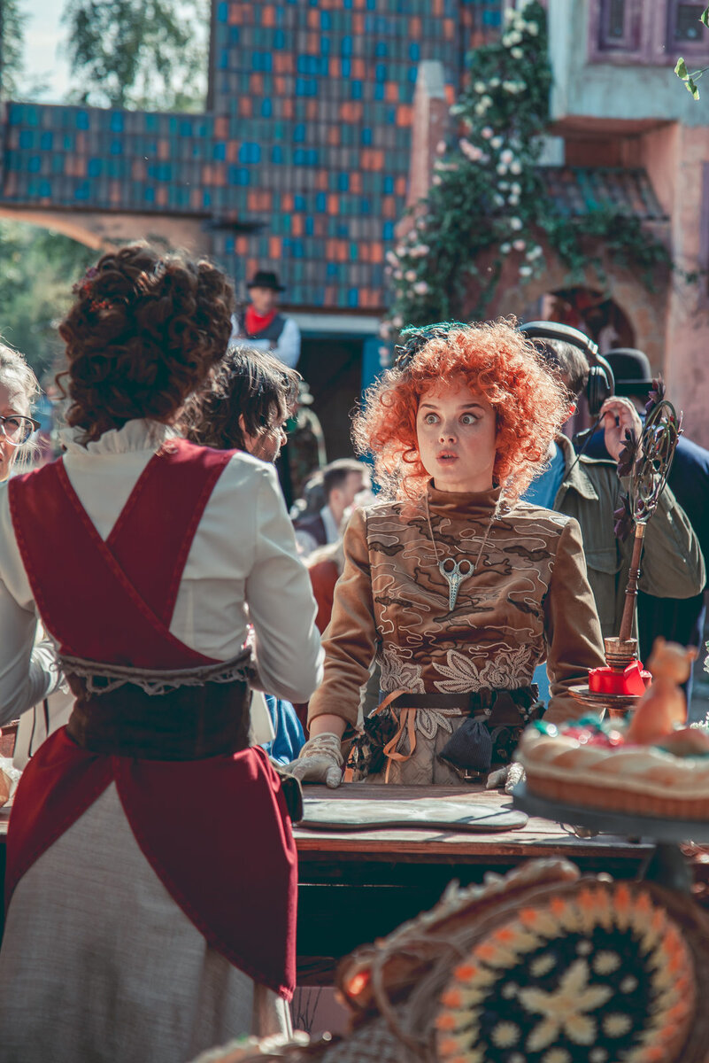 Кадр из фильма. Мама шапочки стоит за прилавком в центре городка.