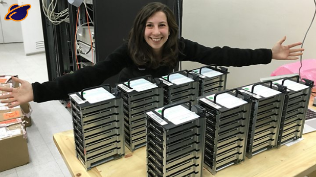 На изображению учёная из Массачусетского технологического института  Katie Boumanove со стопками жестких дисков с данными изображения черной дыры. 
