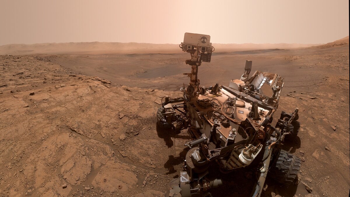 Автопортрет марсохода Curiosity у подножия горы Шарпа. На горизонте виднеется цепочка гор — кольцевой вал кратера Гейла
