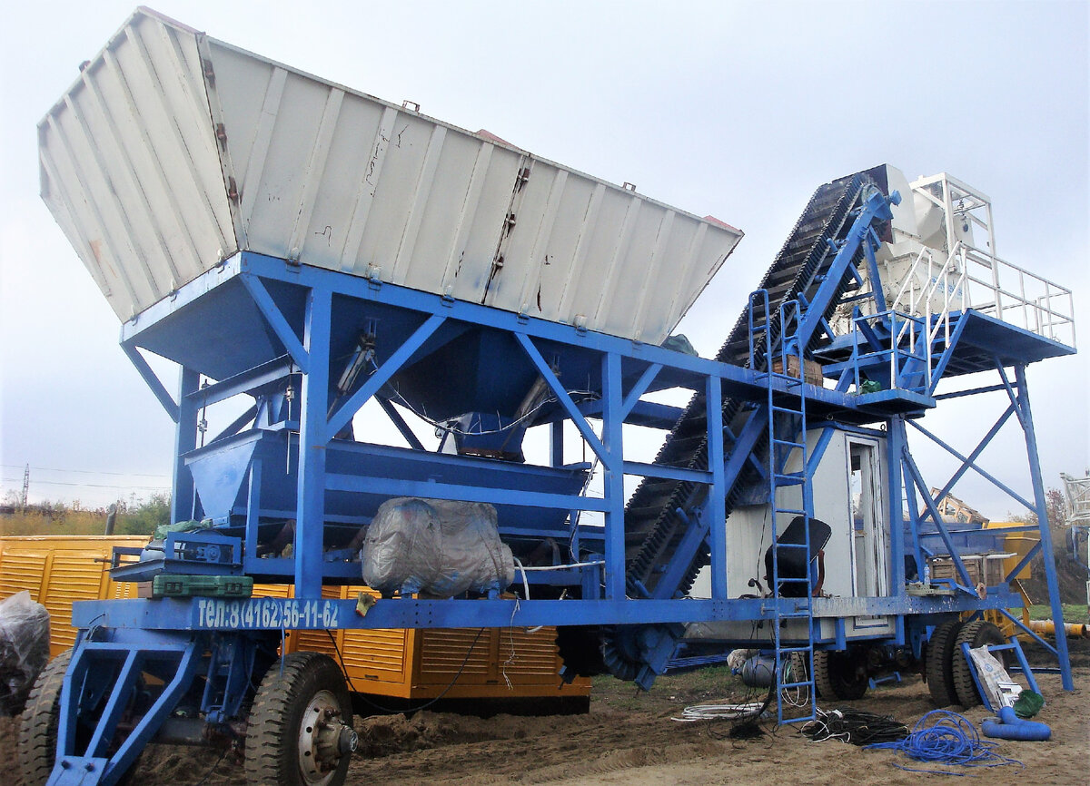 Мобильный бетонный завод, буксируемого типа, тип загрузки инертных материалов в бетоносмеситель - конвейерная лента карманного типа. Бетоносмеситель - двухвальный горизонтальный, принудительный.