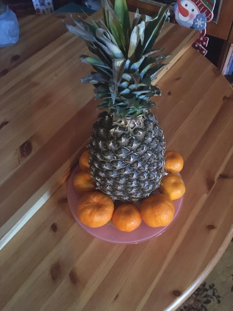 Auf dem Foto können Sie einen groβen Ananas und Mandarinen sehen. 