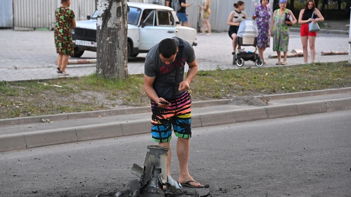    Жители города около неразорвавшегося боеприпаса на месте обстрела Ленинского района Донецка© РИА Новости