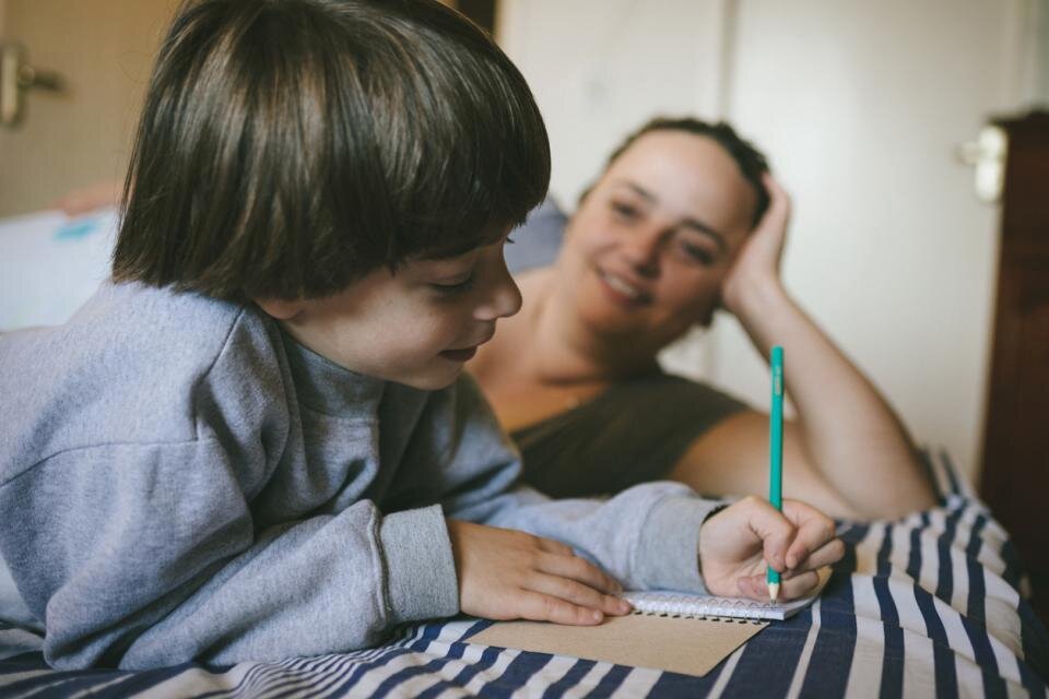 Милый мальчик делает. The boy is doing homework and the mother is watching.