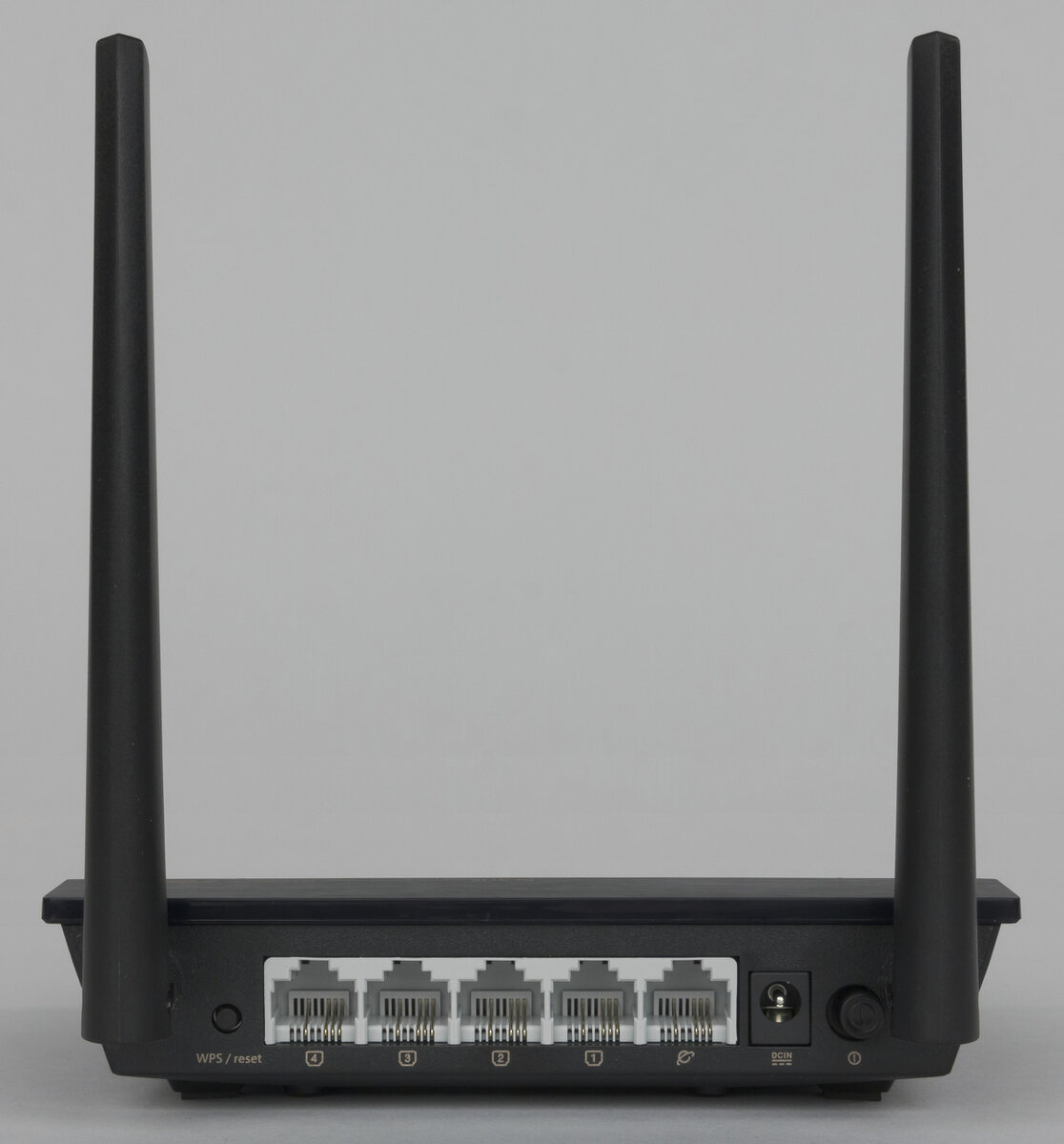 Роутер Asus RT-N11P, вид сзади. Четыре LAN помечены цифрами, WAN значком интернета. Слева кнопка сброса в заводские настройки, справа разъём питания и кнопка выключения.